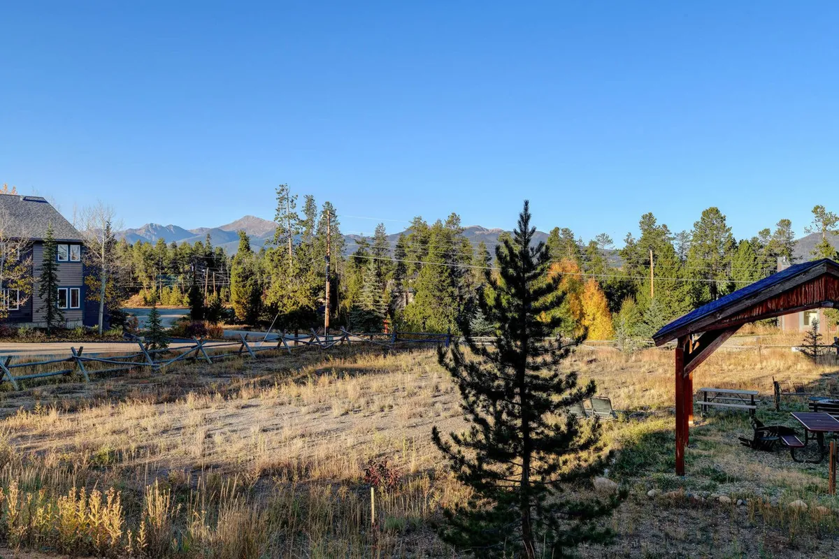 This image captures an expansive grassy area with a wooden pavilion set against the backdrop of a stunning mountain range. The scene highlights opportunities for outdoor recreation such as hiking or picnicking, with the soft light hinting at sunset and a tranquil natural ambiance.