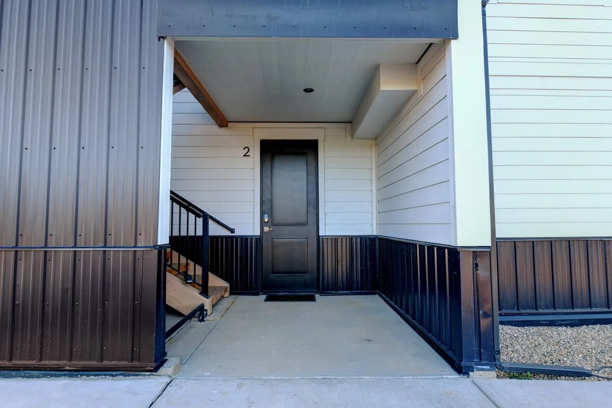 The front door and staircase of the property are visible, with modern metal siding adding contemporary charm. The image invites viewers to imagine arriving at or returning from a day of exploring, highlighting the welcoming aspect of the property.