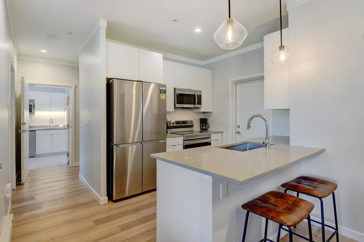A welcoming, modern kitchen featuring stainless steel appliances, a spacious kitchen island with quartz counters, and two bar stools. The area is bathed in natural light, making it ideal for cooking, entertaining, and casual dining.
