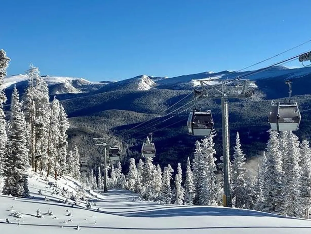 A sweeping view of ski lift gondolas gliding over snow-covered trees with a majestic mountain range in the background. The scene captures the exhilarating spirit of mountain sports and the natural beauty of Winter Park, highlighting opportunities for skiing, snowboarding, and scenic rides.