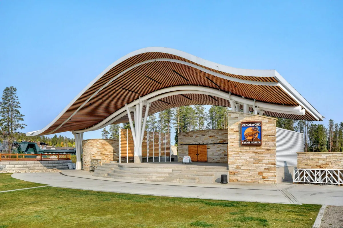 An exterior view featuring a curved roof structure, a stone wall, and wooden accents, set against an outdoor backdrop. The space suggests a welcoming communal environment, possibly at the entrance to a building or a gathering spot, emphasizing the property's connection to the outdoors.