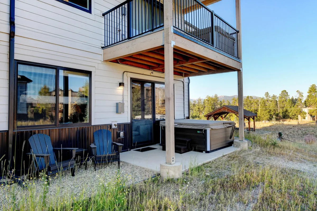 This exterior scene displays a hot tub and a cozy seating area on a patio, with an upper balcony above and expansive landscape views in the distance. The setup is perfect for stargazing, social gatherings, or unwinding after a day outdoors.