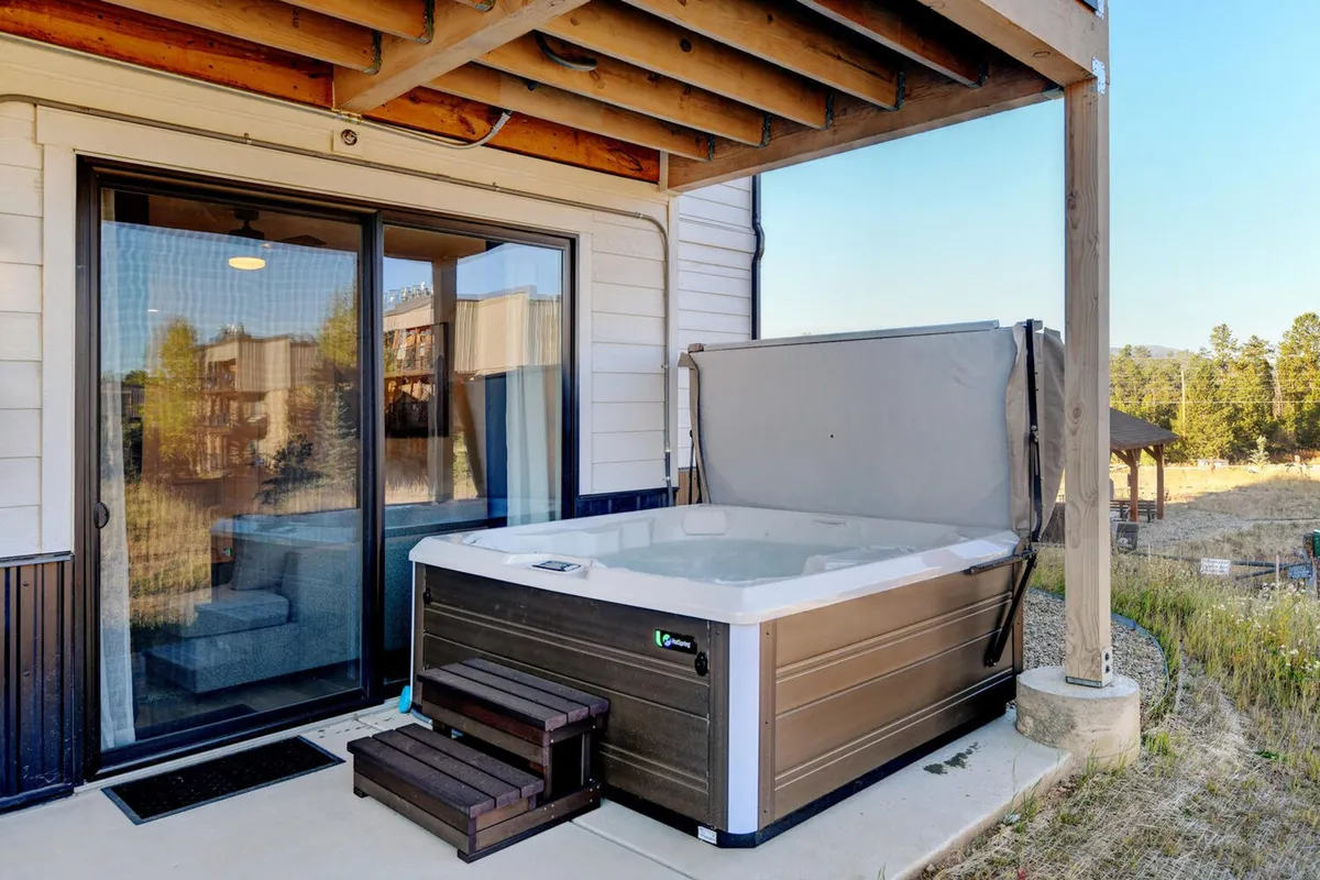 This exterior image features a private hot tub situated on a patio just outside sliding glass doors, set against a backdrop of tranquil mountain scenery. The area is designed for relaxation and socializing, with inviting views that enhance the outdoor experience.
