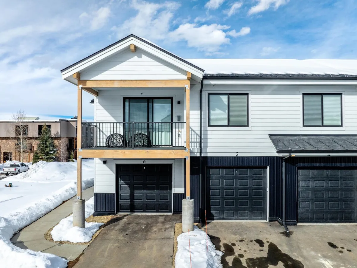This photo features the home's exterior with a cozy balcony, garage doors, snow-covered ground, and a welcoming front entrance. The image captures the essence of winter in the mountains and hints at direct access to the outdoors from the comfort of your condo.